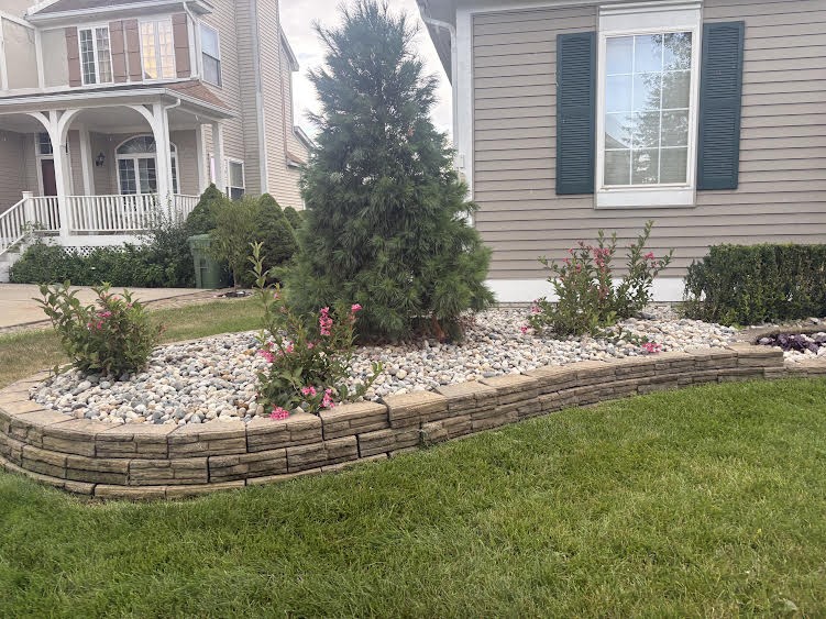 Stone-edged landscape bed filled with river rock and flowering shrubs
